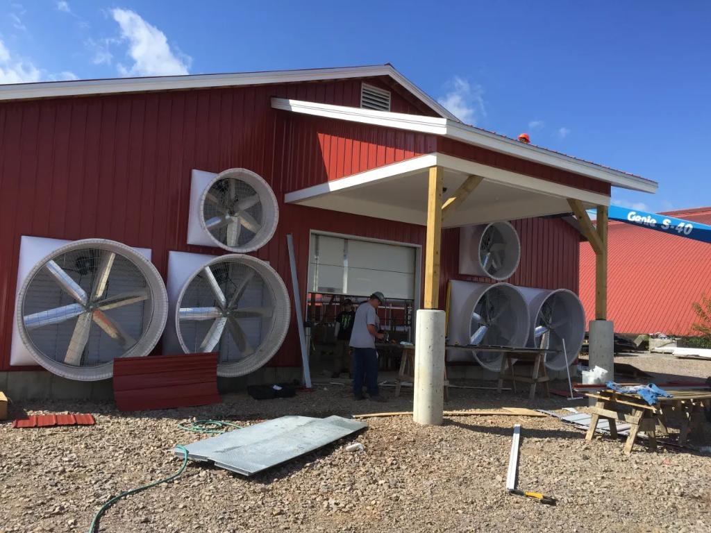 Large ventilation fans being installed on red metal agricultural building